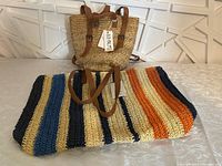 Smaller tan woven handbag with leather straps and a Beachly tag attached, standing upright.