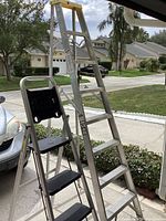 Two aluminum ladders standing on driveway, one tall extension ladder around 8 ft, and a shorter step ladder around 5.6 ft with black steps and tool tray.