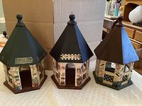 Photo showing three hexagon-shaped, hand painted birdhouses with peaked roofs and decorative details including signage.