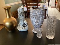 Photo showing five vases on a table in a home setting: gold-tone metal, ceramic with boy, textured mottled ceramic, small glass flower-shaped, tall glass with raised ovals.