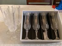 Set of 7 Longchamp crystal champagne flutes arranged with 4 new in original box and 3 standing outside the box.