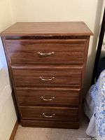 Front view of a brown child dresser showing four drawers with metal handles. Minor scratch visible on the top edge.