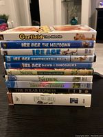 Stacked DVDs showing titles and cases of 10 children's movies including Ice Age series, Shrek series, Garfield, Polar Express, and Five Mile Creek.