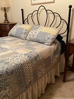 Black metal full size bed with cloud design headboard, patchwork floral comforter, two matching shams, and white bedskirt, viewed from side angle