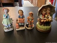 Four porcelain figurines on table including two Goebel marked and two unmarked, one music box figurine without key, made in Japan.