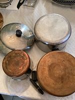 Top view of three pots showing lids and handles on white quilted surface.