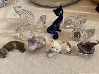 Overview of the 10 cat figurines showing clear glass, blue and black glass, painted ceramic, and resin pieces