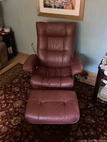 Photo showing brown leather rocker recliner chair and matching ottoman footstool, highlighting padded segmented cushions and wooden round bases