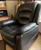 Front and angled view of black leather lift chair showing padded seat, backrest with segmented cushions, and armrests with white stitching detail.