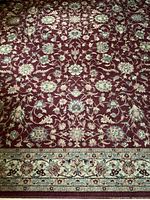 Close-up photo of the Shaw ornamental rug showing floral pattern and border detail on reddish-burgundy background.