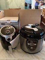 Cosmo COS-23AFAKB Air Fryer and Elite EPC 608 Electric Pressure Cooker shown side by side on table with air fryer box in background