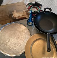 Lot items arranged on surface: 2 woks (one Nordic Ware), 2 metal serving trays (silver scalloped and gold-tone), vintage smoky plastic recipe box, Everactive blue flashlight, and 2 exercise stretch bands (green and red).