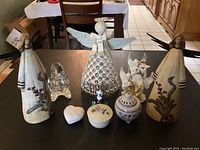 Photo showing seven angel figurines and three small trinket boxes including Lenox collectors items on a black tabletop with dining room in background