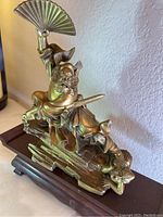 Front angle view of brass ghost catcher statue on wooden stand showing detailed facial features and posture.