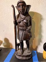 Full view of carved wood figure of a woman holding a walking stick with a small dog at her side.