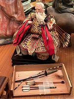 Carved seated figurine dressed in ornate robes with miniature arrows and bow in front