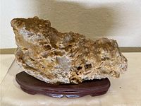 Front view of the crystal layered rock on its wooden stand, highlighting the texture and coloration of the rock.