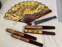 Six folding fans displayed, one open showing detailed Asian-style artwork, others folded with different designs.
