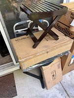 Photo showing wooden folding shower stool stacked on closed cardboard boxes on a patio.