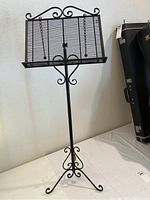 Full view of black metal adjustable music stand showing scroll design on top and tripod base.