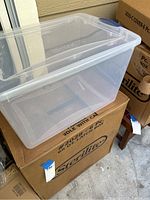 Clear Sterilite 66 quart storage box with lid placed on top of brown Sterilite box packaging.