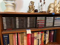 One shelf of music CDs stored in two plastic cases on a wooden shelf, with a collection of books below.