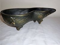 Side view of the ornate metal dish showing embossed pattern and bathtub shape with feet.