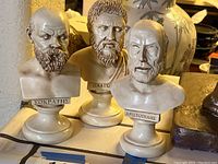 Photo showing three bust figurines of Greek philosophers Socrates, Plato, and Aristotle on a surface, providing an overall view of the lot.