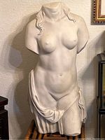 Front and side views of the white composite material female torso statue figure, showing detailed draped cloth and hair locks. No head, arms, or legs present.