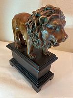 Front angle showing the carved wooden lion on a rectangular black base, highlighting the face and mane details.