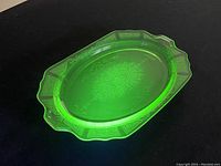 Perspective view of the green uranium glass plate showing detailed etched floral and border designs, glowing under UV light.
