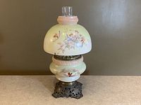Full view of the lamp showing the milkglass painted shade with cherubs and floral design, atop the detailed brass base.