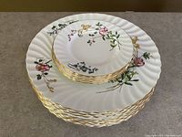 Stack of 8 white porcelain dinner plates with floral sprays and gold scalloped rim.