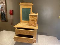 Front view of early wooden gentleman's dresser showing large framed mirror, two lower drawers opened, and elevated storage compartment on top.