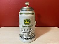 Front view of the ceramic stein showing John Deere logo and tractor emblem in relief.