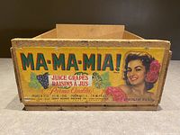 Front side of vintage wooden crate showing colorful Ma Ma Mia branding, grapes, pineapple images, and woman's portrait.