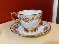 Teacup and saucer displayed showing floral design and gold detailing.