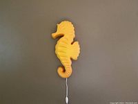 Full view of the orange seahorse light hanging on the wall, showing the power cord with inline switch.