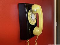 Side view of the black and yellow vintage rotary wall phone showing yellow handset and rotary dial with clear lucite overlay.