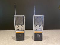 Front view of two Outsider Fanon Outrider CB transceiver walkie talkies side by side, showing ribbed grills, control knobs, and antennas.