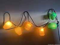 Lit patio string lights with multi-colored plastic lantern covers in yellow and green, shown decoratively hanging.