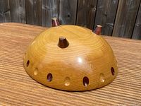 Close-up image of underside of large wooden salad bowl showing three conical legs and thumbprint inlays around edge.