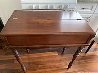 Overview photo of antique wooden desk with fold back top closed, showing rich brown wood finish and turned legs.