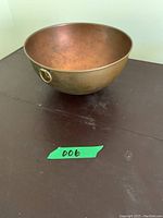 Side view of round copper bowl with metal ring attached, placed on dark surface.