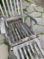 Front angled view of the wooden lounge chair showing the broken seat slat circled in blue, weathered finish, and brass-tone metal brackets on the sides.