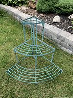 Photo of green metal corner garden shelf on grass, showing single unit with three quarter-circle shelves.