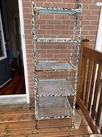 Front view of the five shelf metal garden stand with visible signs of wear and one shelf repaired.