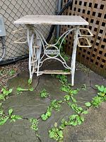 Front view of the white painted Raymond sewing machine base with marble top on stone patio outdoors