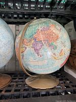 Single globe with brass-colored metal semi-meridian and base, detailed world map in pastel colors.