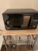 Small black microwave on a metal rack with front view showing digital keypad and door design.